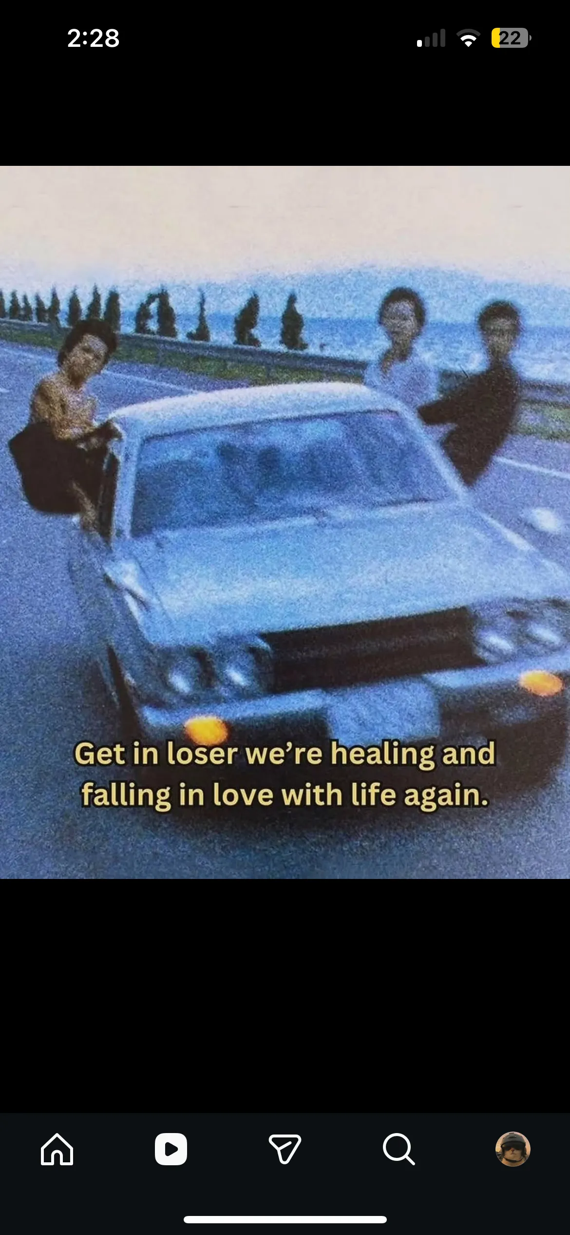 Phone screenshot of a grainy photo of three people around a car on a seaside road, captioned: Get in loser we’re healing and falling in love with life again.