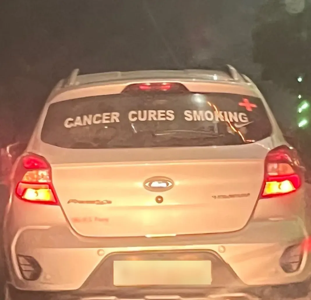 Photo of a car’s rear window with a sticker reading CANCER CURES SMOKING
